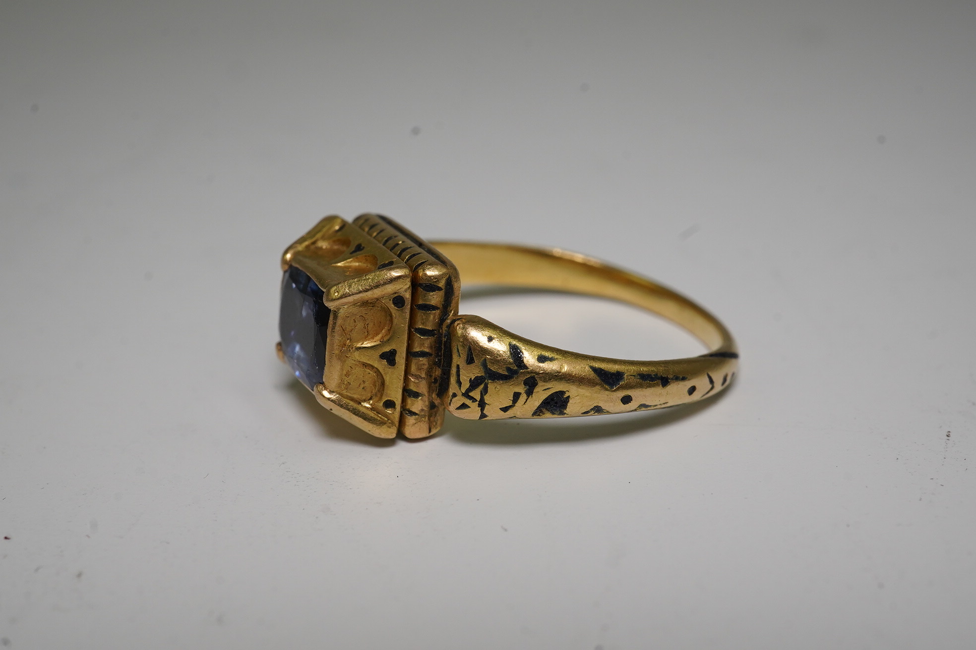 An antique high carat gold, black enamel and collet set cushion cut sapphire set 'poison' ring